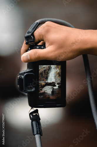 Hand holding camera which taking photo of beautiful waterfall.