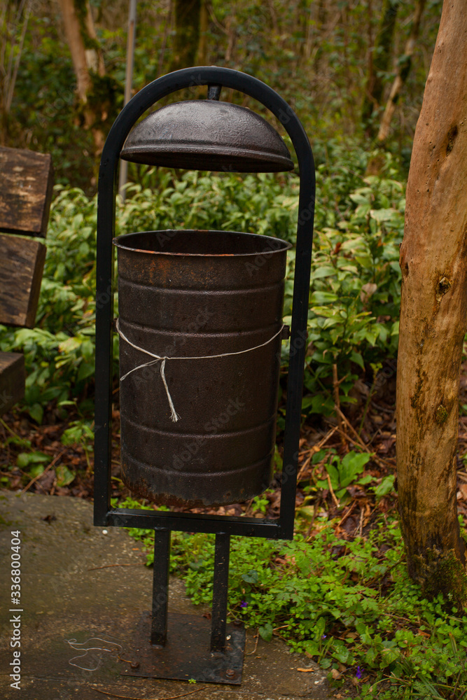 Black garbage bin in the forest on green background in a recreation area Black garbage bin in the forest on green background in a recreation area