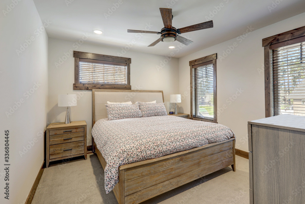 Fototapeta premium Natural tones cozy bedroom interior with grey bedding, beige carpet and lots of windows.