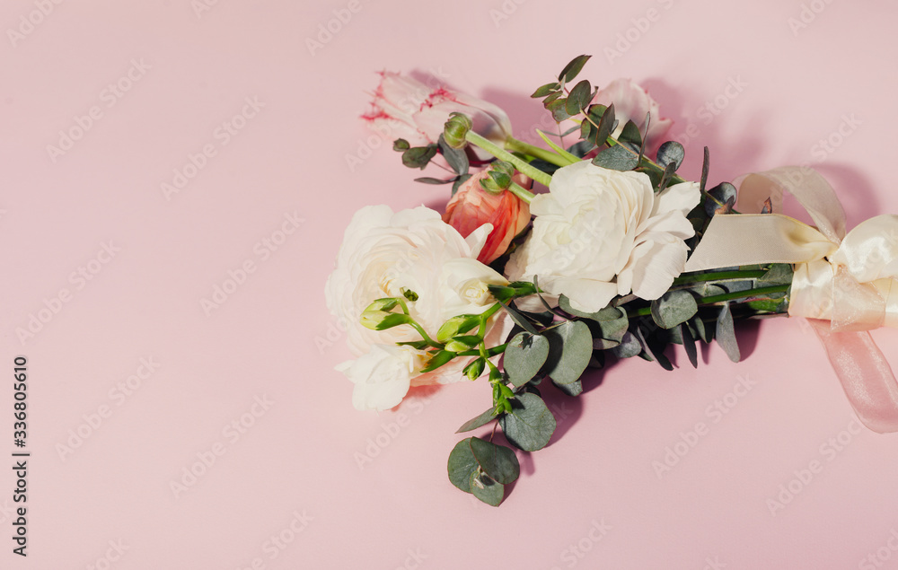 A top view of a bride bouquet of flowers on pink background. Tulip, eucalyptus branches, white Ausin roses and ranunculus with tape. Copy space