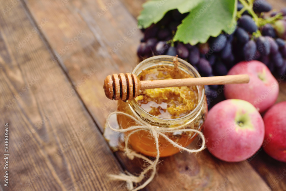 honey in a beautiful jar, wooden spoon spindle, grapes and apples on a wooden background