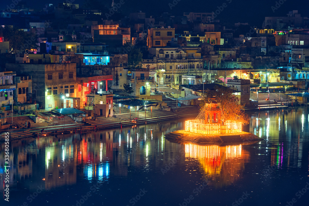 View of famous indian hinduism pilgrimage town sacred holy hindu religious city Pushkar with Brahma temple, aarti ceremony, lake and ghats illuminated at sunset. Rajasthan, India. Horizontal pan
