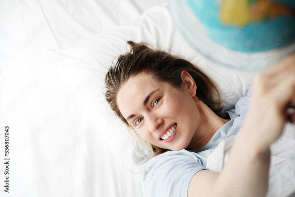 Beautiful woman dreaming about vacation. Girl holds in hand a small globe and laying in the bed. Beautiful woman dreaming about vacation. Girl holds in hand a small globe and laying in the bed.