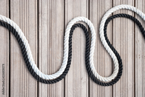 Black and white nautical ropes curving together outdoors on a wooden background