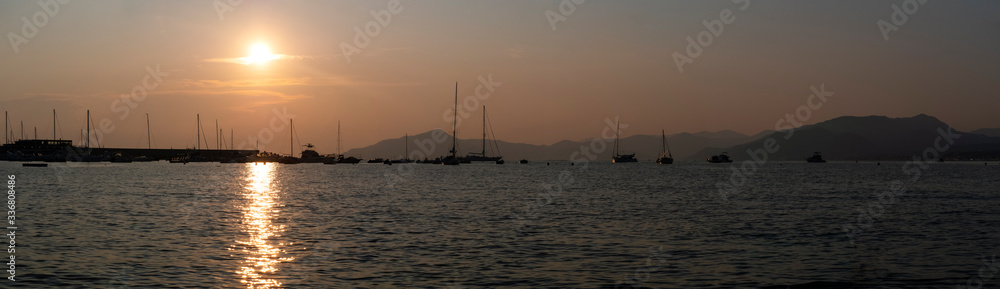Sunset at sea. Yachts without sails are at the pier. Mountains on the horizon. A sunny path glistens on the sea. Panorama. Beautiful background.