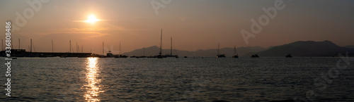 Sunset at sea. Yachts without sails are at the pier. Mountains on the horizon. A sunny path glistens on the sea. Panorama. Beautiful background. © Svetlana