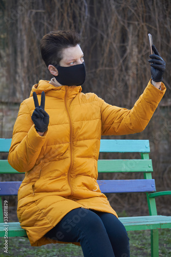 Middle aged european woman in protective black mask and gloves takes selfie on smartphone outside during coronavirus COVID-19 Epidemic photo