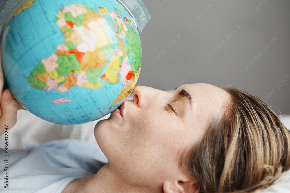 Portrait of young woman laying in bed and kissing globe. Horizontal.
