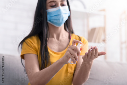 Coronavirus prevention. Young girl in medical mask applying sanitizer on her hands at home
