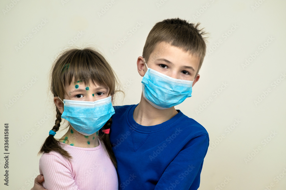Boy and girl wearing blue protective medical mask ill with chickenpox, measles or rubella virus with rashes on body. Children protection during epidemic of coronovirus. Covid-19 contagion concept.