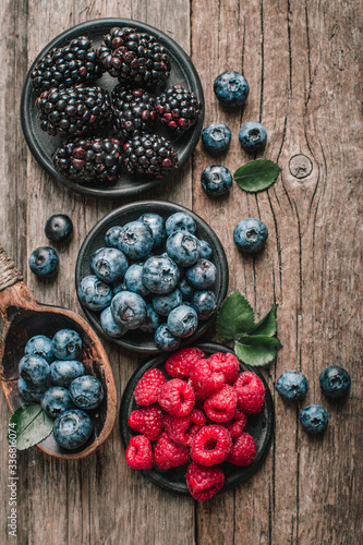 Fresh berries with raspberries, blueberries, blackberries in bowl on a stone stand on wood background.