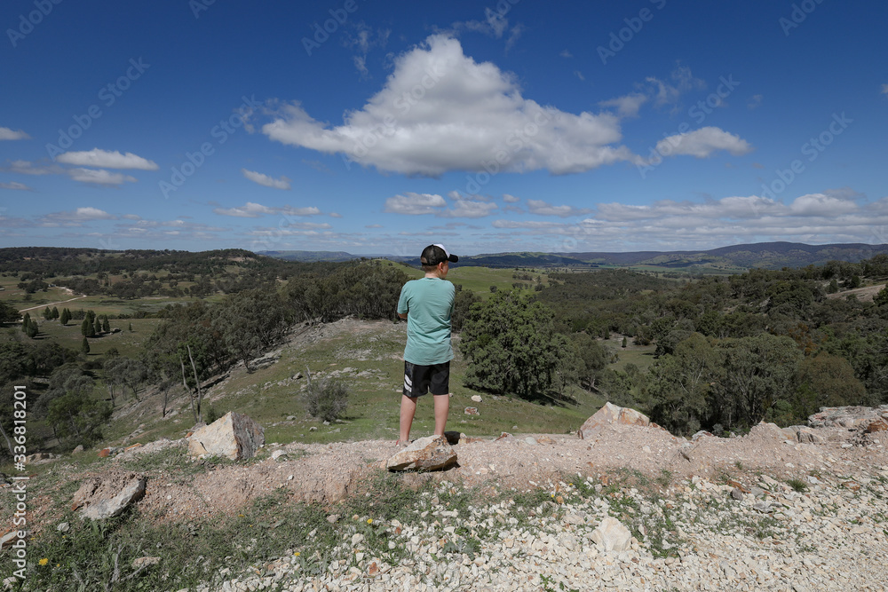 Boy standing on rocky cliff edge admiring view of landscape below