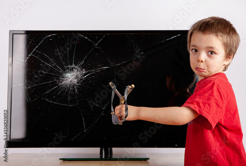 Photos Shocked little boy standing in front of a TV with broken screen and showing his slingshot