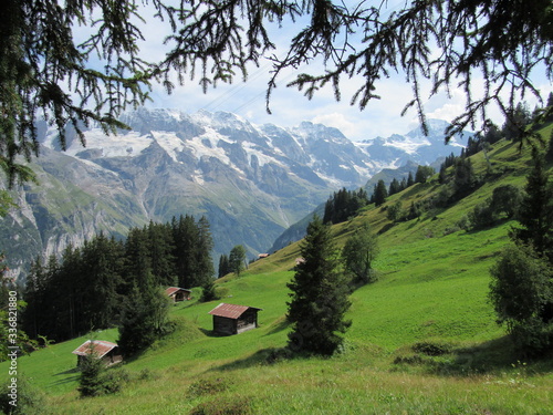Small cabins sit on a Switzerland hillside near Murren with towering mountains in the background. The unused ski-lifts run overhead.
