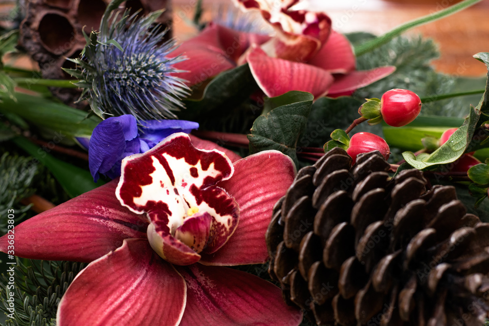 Winter bouquet of cymbidium, eringium,hypericum,nobilis,iris,cones and dry Lotus inflorescence on the brown wooden table