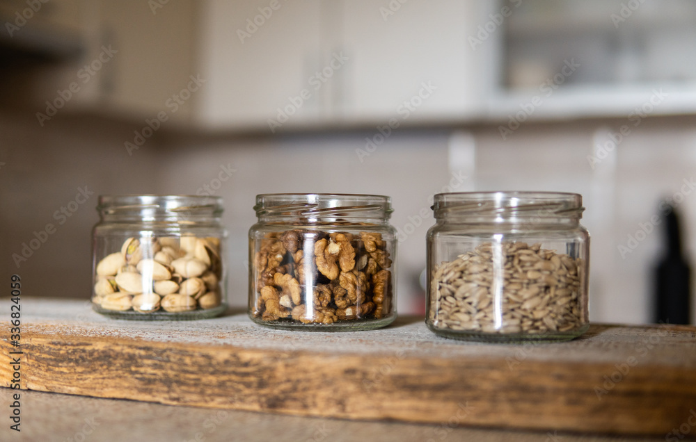 Sunflower seeds, walnut and pistachio in a jars which standing on a white vintage table with a kitchen on background. Nuts is a healthy vegetarian protein and nutritious food. Nuts on rustic old wood. Sunflower seeds, walnut and pistachio in a jars which standing on a white vintage table with a kitchen on background. Nuts is a healthy vegetarian protein and nutritious food. Nuts on rustic old wood.