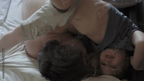 little boy wake up their dad.  Cute toddler son and father sleeping together on bed in bedroom at home.