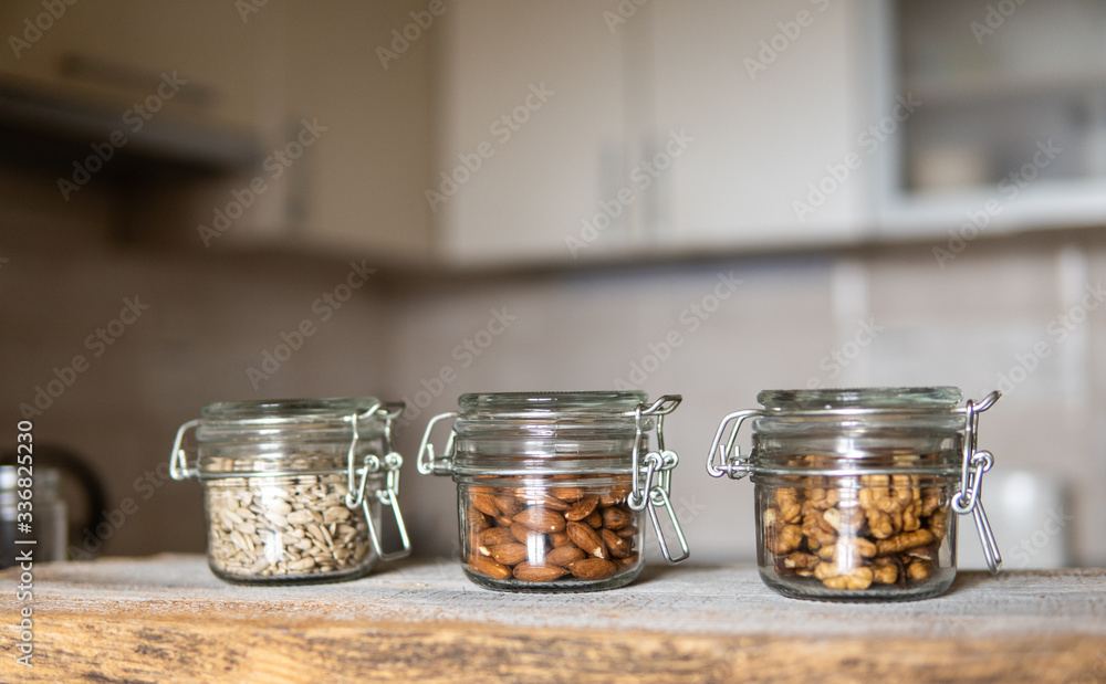 Sunflower seeds, walnut and almond in a jars which standing on a white vintage table with a kitchen on background. Nuts is a healthy vegetarian protein and nutritious food. Nuts on rustic old wood. Sunflower seeds, walnut and almond in a jars which standing on a white vintage table with a kitchen on background. Nuts is a healthy vegetarian protein and nutritious food. Nuts on rustic old wood.