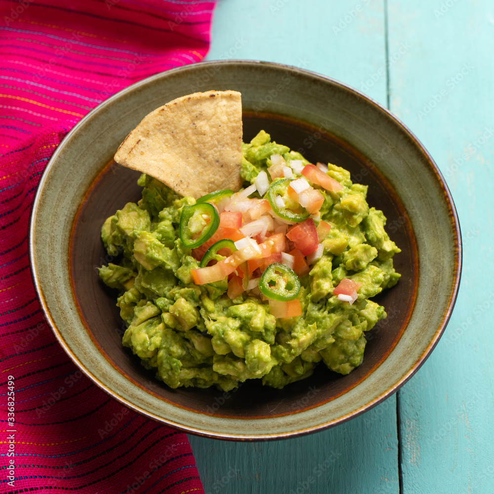Mexican guacamole with tomato and serrano pepper on turquoise background