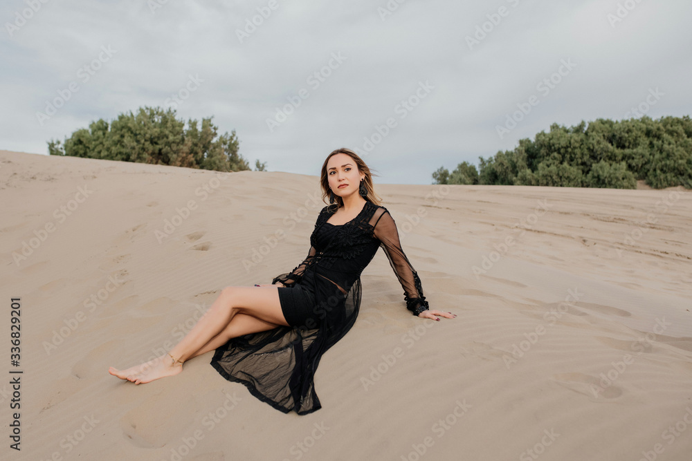 Mujer elegante con vestido negro sentada sobre la arena en la
