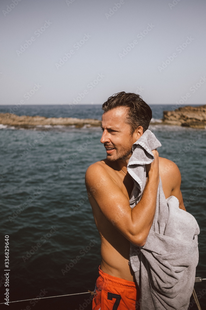 Man looking away while drying with towel at beach against sky on sunny day Man looking away while drying with towel at beach against sky on sunny day