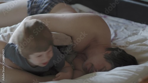 little boy wake up their dad.  Cute toddler son and father sleeping together on bed in bedroom at home.