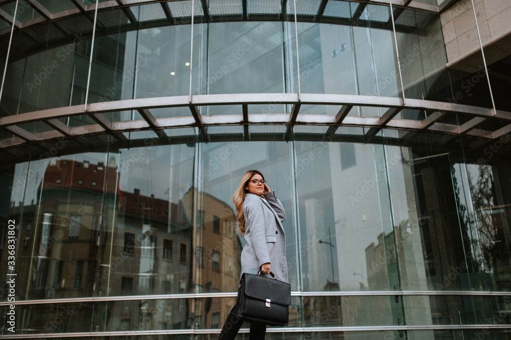 Young attractive caucasian businesswoman with bag walking in front of company Young attractive caucasian businesswoman with bag walking in front of company