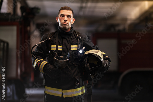 firefighter portrait wearing full equipment and emergency rescue equipment. taking off oxygen mask all sweaty after successful intervention. fire trucks in the background.
