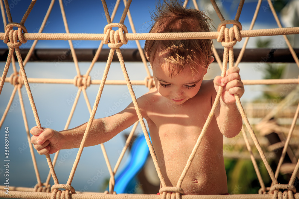 Cute toddler playing in playground at Cancun beach, covered by sand on a suspension bridge. Cute toddler playing in playground at Cancun beach, covered by sand on a suspension bridge.