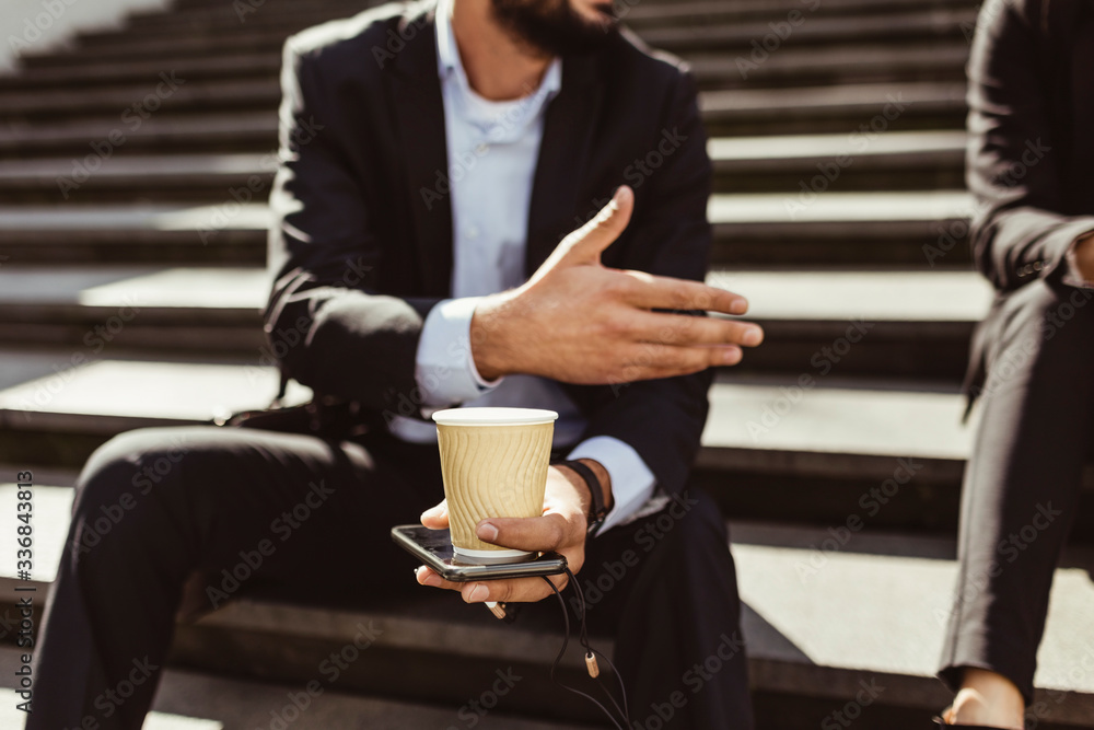 Midsection of businessman with disposable cup making hand gesture while sitting on staircase Midsection of businessman with disposable cup making hand gesture while sitting on staircase