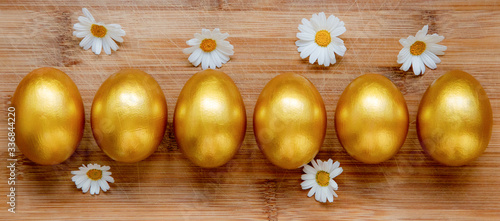 Ester golden eggs and daisies on wooden rustic table.