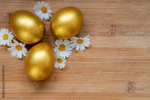 Ester golden eggs and daisies on wooden rustic table.