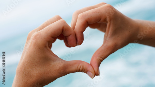 love sign on blue ocean water background. female hands show a symbol