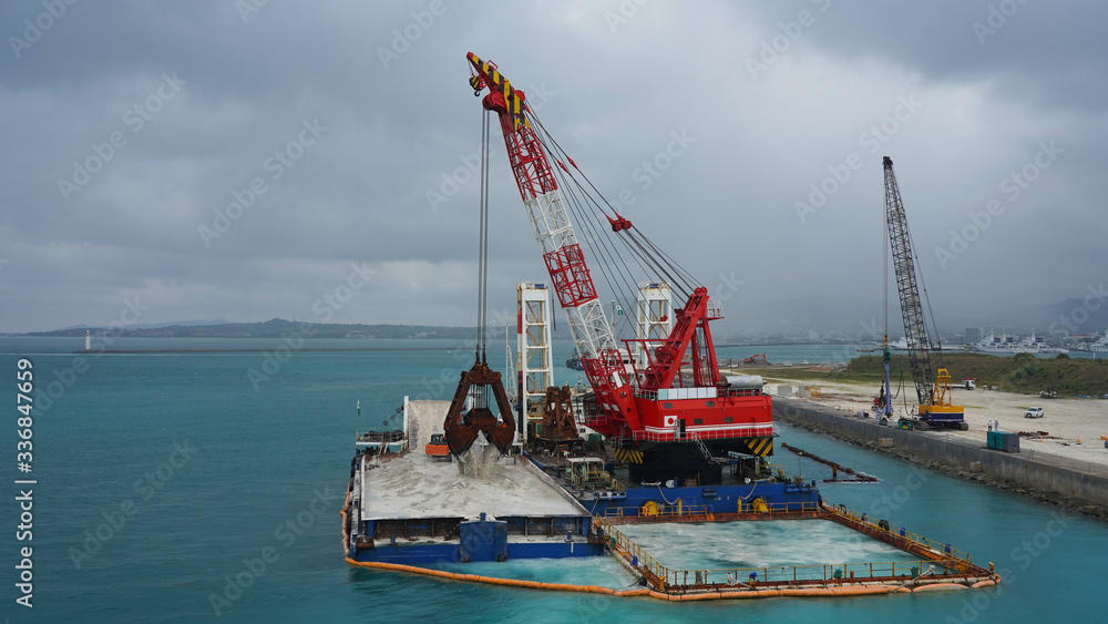 Floating crane platform with a huge bucket extracts sand from the bottom of the Pacific Ocean.
a huge crane extracts white sand from the ocean off the coast of Okinawa.