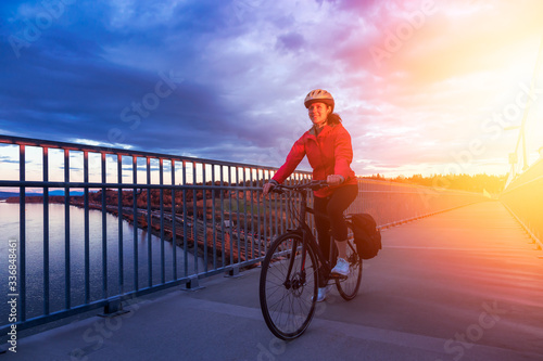 Caucasian Woman riding a Bicycle on a path at Port Mann Bridge during vibrant Sunset. Taken in Surrey, Vancouver, British Columbia, Canada. photo