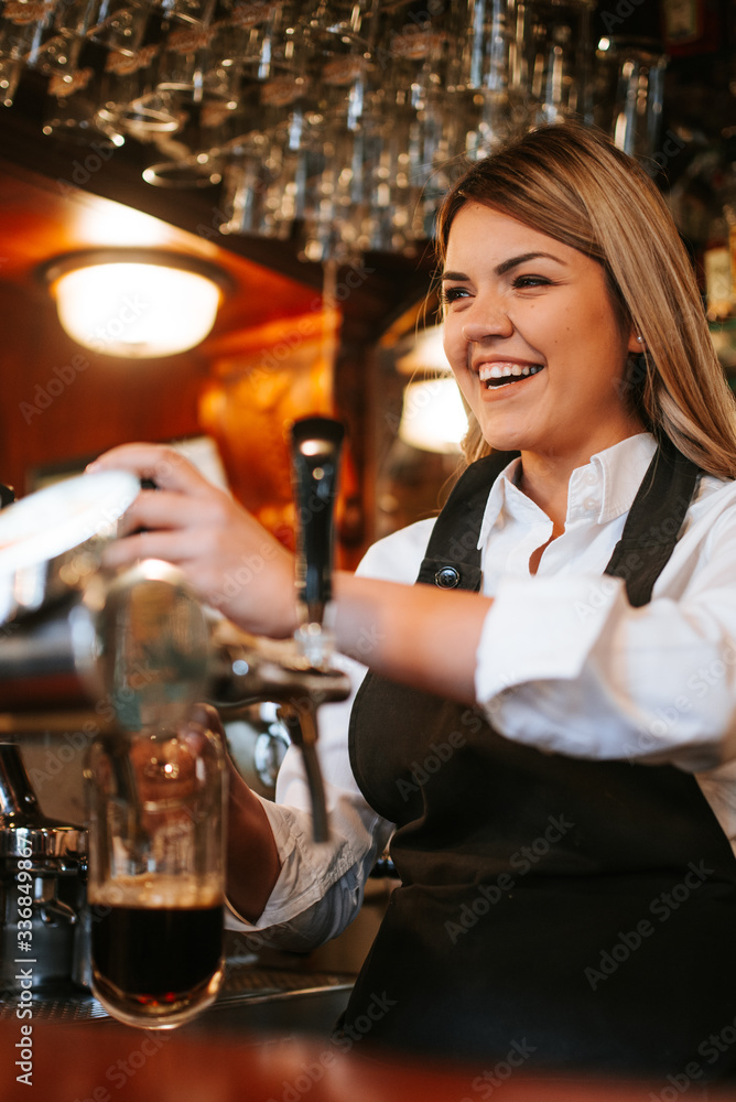 A young attractive blonde caucasian  waitress pouring beer in a cafe