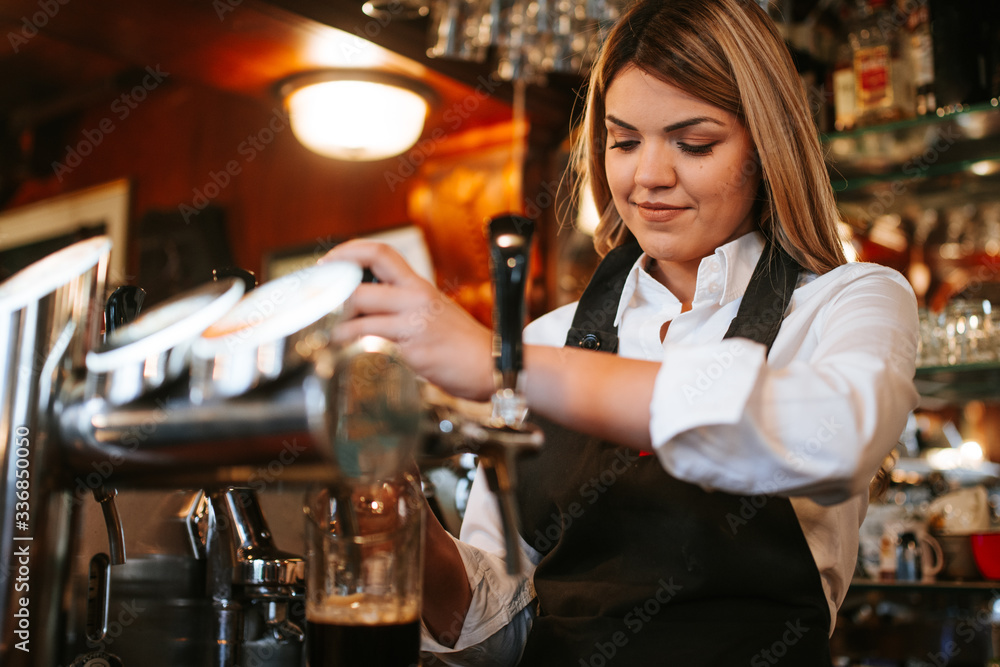 A young attractive blonde caucasian  waitress pouring beer in a cafe