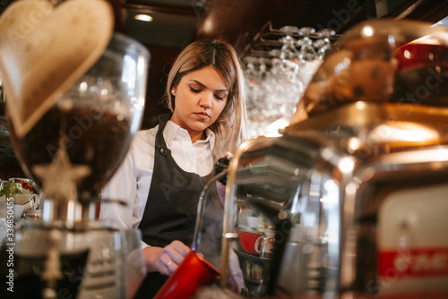 A young attractive caucasian blonde waitress makes coffee in a cafe © Dragica