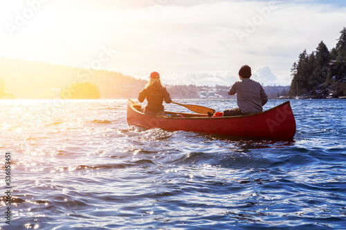 Couple friends on a wooden canoe are paddling in water during a vibrant sunny day. Taken in Indian Arm, near Deep Cove, North Vancouver, British Columbia, Canada. Concept: Adventure, Sport, Explore
