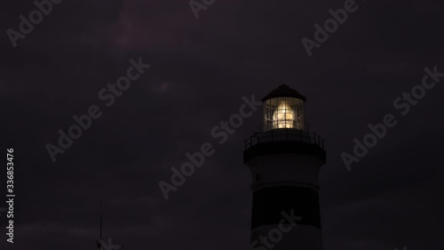 Lighthouse rotating light shining through lens of lantern room on dark, cloudy night