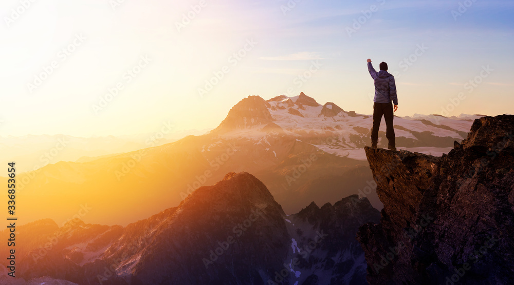 Composite. Adventurous Man Hiker With Hands Up on top of a Steep Rocky Cliff. Sunset or Sunrise. Landscape Taken from British Columbia, Canada. Concept: Adventure, Explore, Hike, Lifestyle