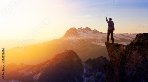 Composite. Adventurous Man Hiker With Hands Up on top of a Steep Rocky Cliff. Sunset or Sunrise. Landscape Taken from British Columbia  Canada. Concept  Adventure  Explore  Hike  Lifestyle