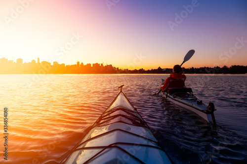 Adventurous Girl Sea Kayaking during a vibrant winter sunrise with City Skyline in Background. Taken in Downtown Vancouver, British Columbia, Canada. Concept: Adventure, Holiday, Vacation, Sport