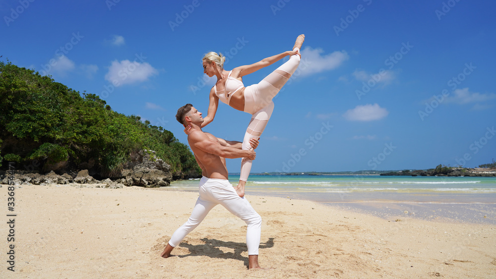 Obraz premium couple of beautiful dancers on the shore of a paradise beach perform acrobatic pose and split