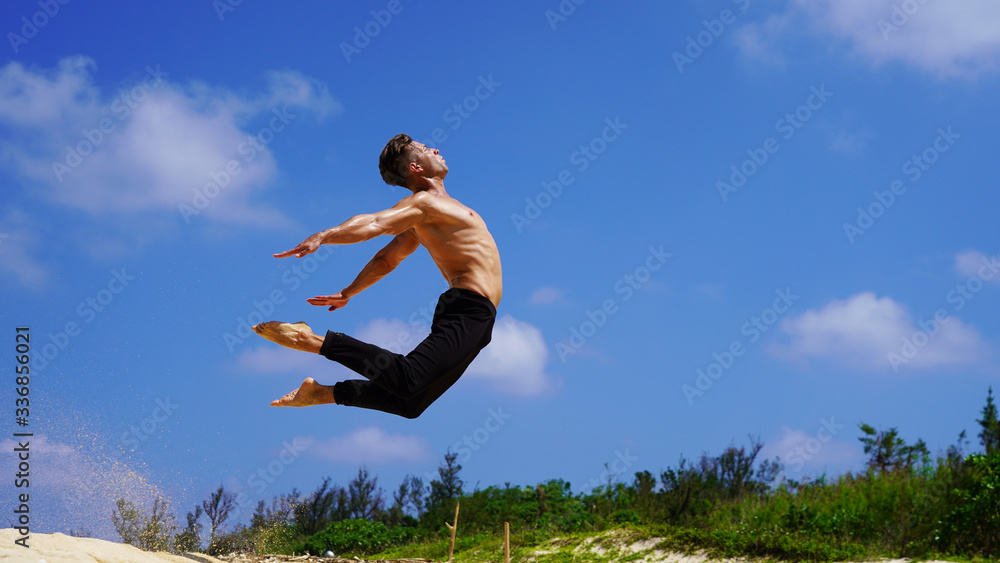 young sporty european guy jumping acrobatics twine. muscular man on the beach shows flexibility back in jumping on background blue sunny sky. stretching young sporty european guy jumping acrobatics twine. muscular man on the beach shows flexibility back in jumping on background blue sunny sky. stretching