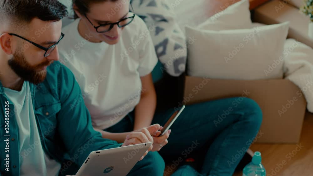 the young attractive couple of just married people sitting on the floor and looking at the tablet of their new home, thinking about design. Indoor the young attractive couple of just married people sitting on the floor and looking at the tablet of their new home, thinking about design. Indoor