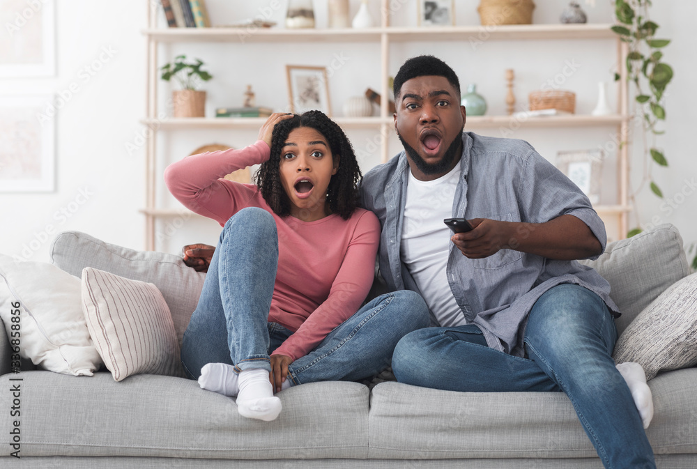 Coronavirus News. Shocked african american couple watching tv with open mouth Coronavirus News. Shocked african american couple watching tv with open mouth