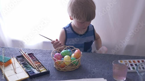 Little blond kid boy coloring eggs for Easter holiday in bath room, indoors. Child holding basket with painted eggs. Child having fun and celebrating feast with easter toy bynny photo