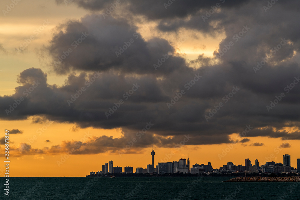 Cityscape, landscape, view of sea with a city at the horizon at twilight before sunset. View of Pattaya city from    Jomtien Beach with orange sky and heavy black cloud.