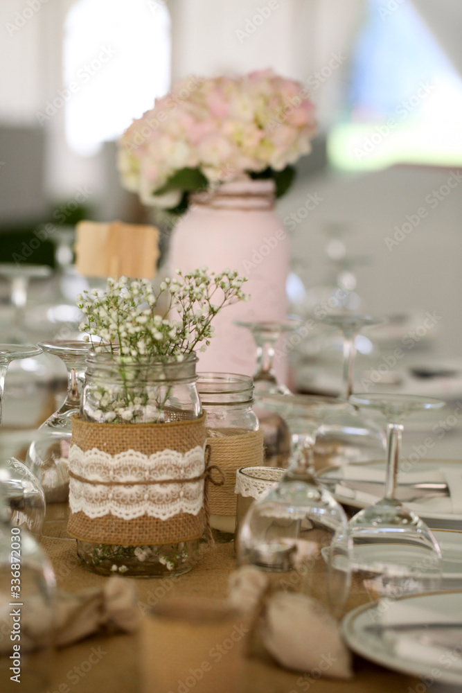 A soft country wedding table setting with flowers in vases and burlap trim.